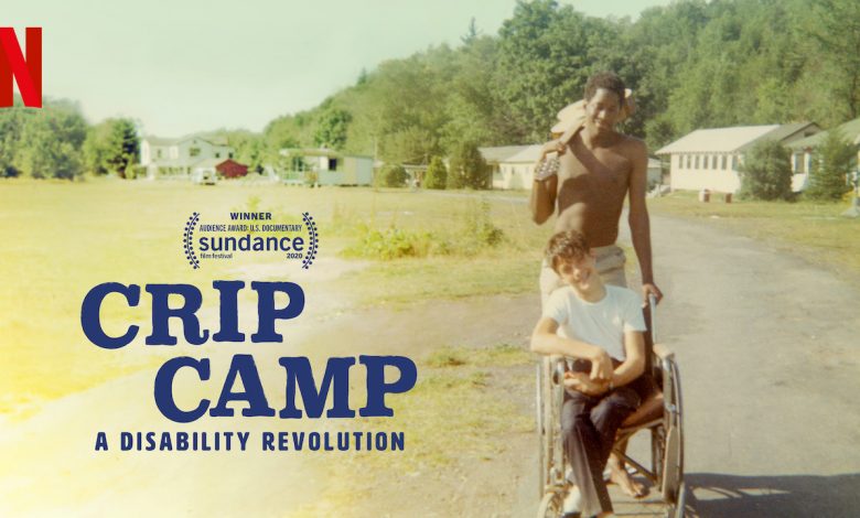 Image from the movie Crip Camp, a Disability Revolution: Young African American man pushing young white man in wheelchair while holding guitar.